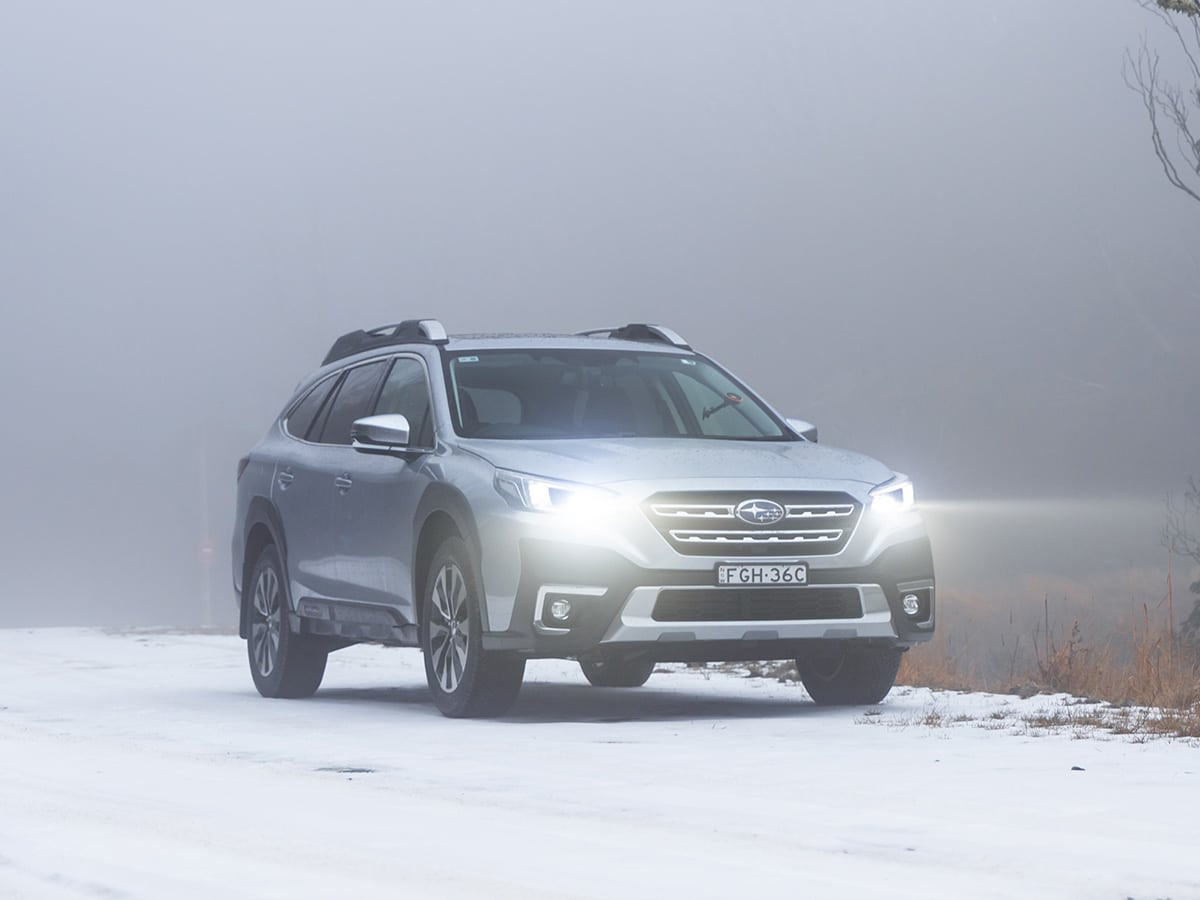 Subaru Outback di chuyển trên nền tuyết với đèn pha chiếu sáng